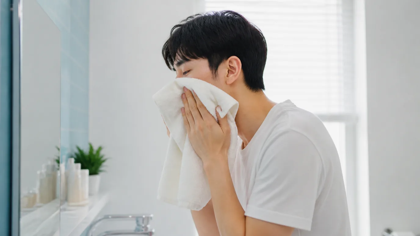세면대 앞에서 수건으로 얼굴을 조심스럽게 닦는 남성