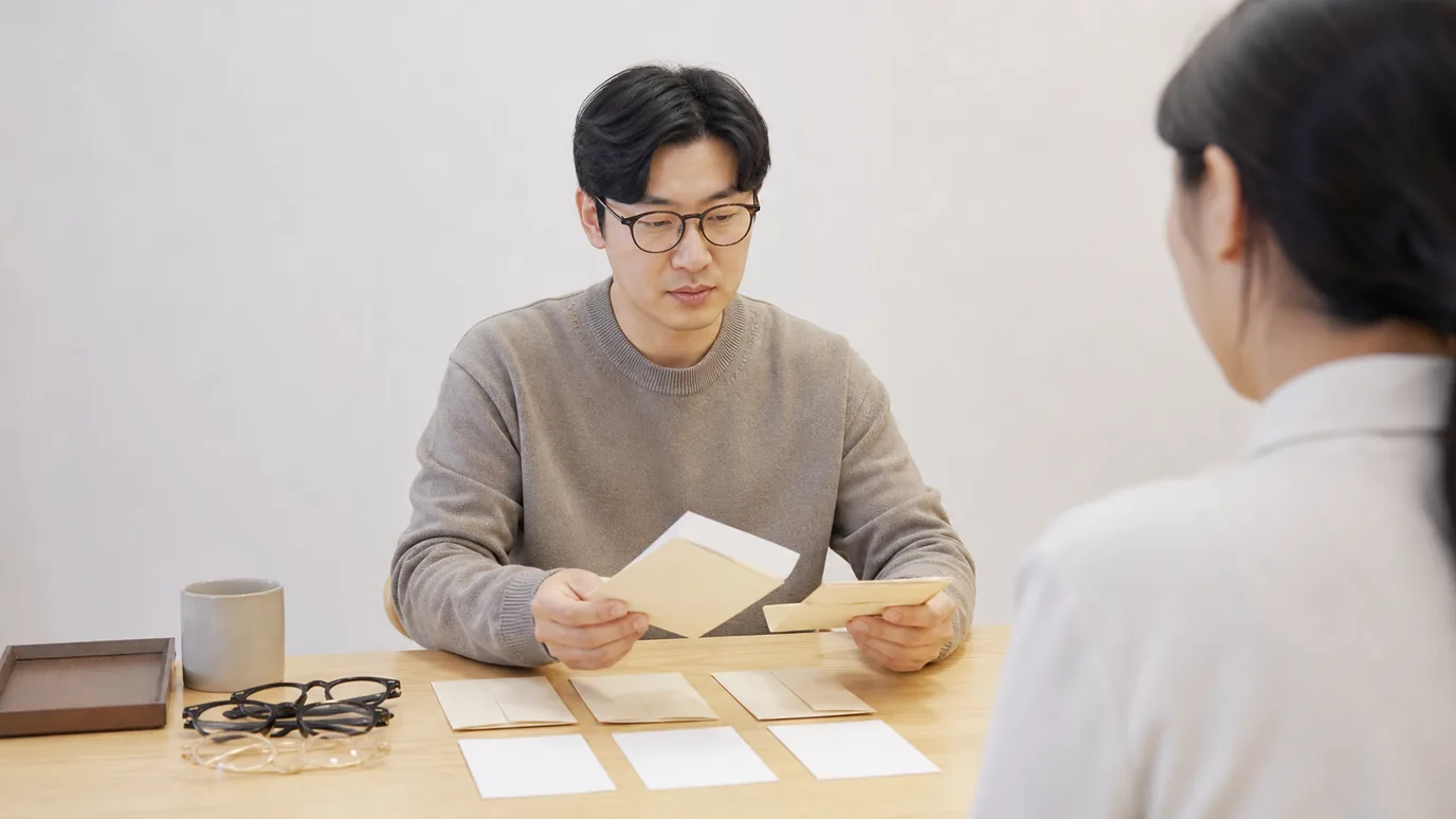 밝은 상담 테이블에서 30대 한국인 성인이 서로 다른 날짜의 봉인 견적서와 눈별 계획 카드를 맞춰 보는 장면