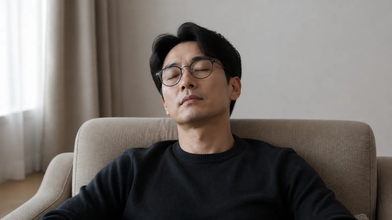 자연광이 드는 방에서 30대 한국인 성인이 안경을 쓴 채 눈을 편안히 감고 쉬는 장면